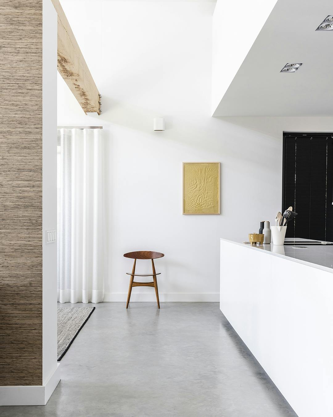 Tussen de keuken en de eetkamer staat een vintage CH33-stoel van Carl Hansen, die tegenwoordig weer in productie is. De kunst aan de wand is van Fant, de lamp erboven is van Modular. CH33 Carl Hansen, betonnen vloer en wit kookeiland