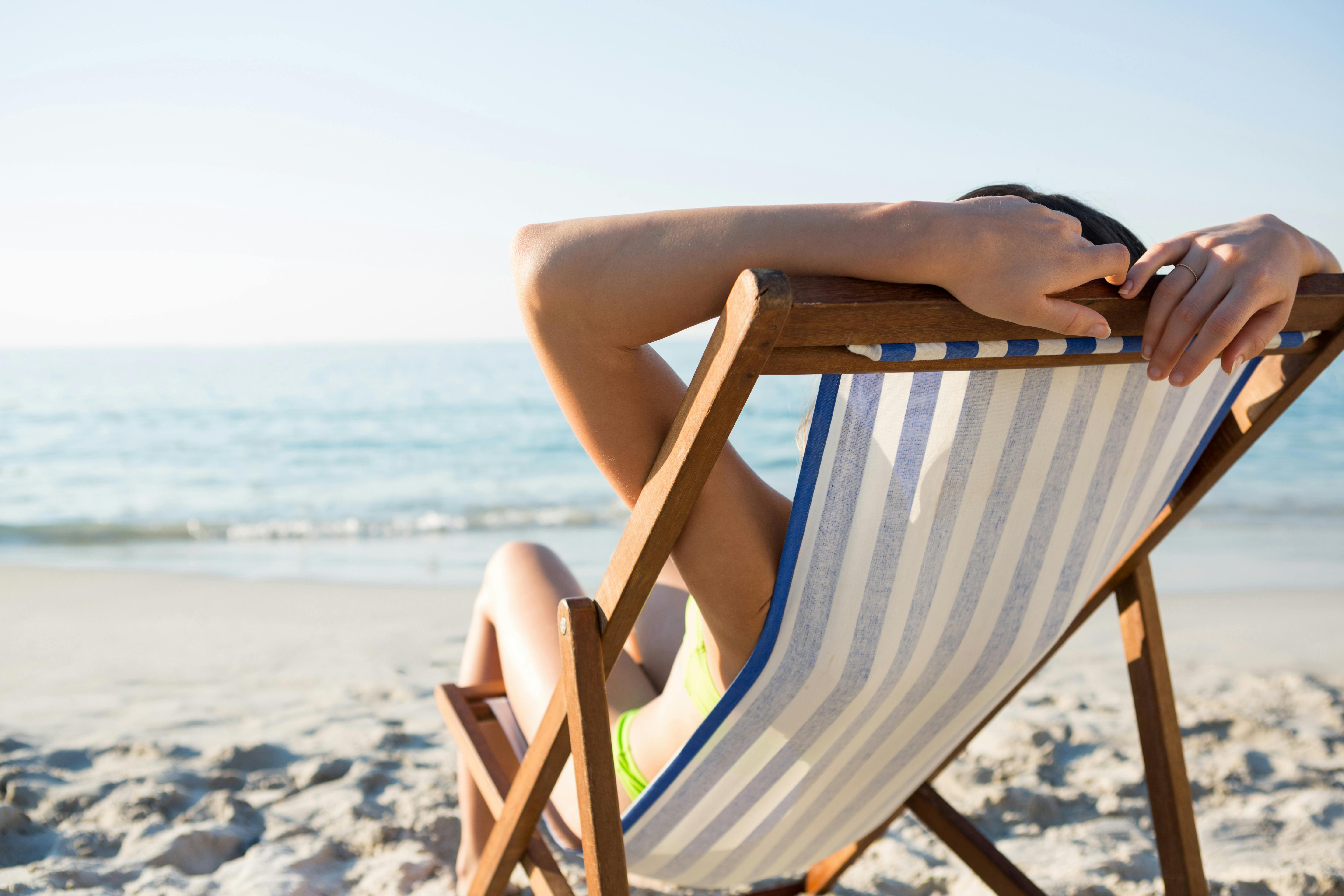 Med menstruationskoppen kan du bekymringsfrit hoppe i bikinien eller badedragten. Kvinde ligger i en solstol på en strand.