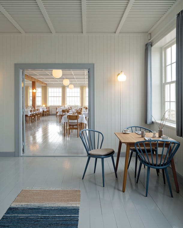 Naast de natuurkleuren, hebben de ruimtes allemaal verschillende kleuren gordijnen die verwijzen naar de geschiedenis van het gebouw. Svinkløv badehotel restaurant entree met wit hout