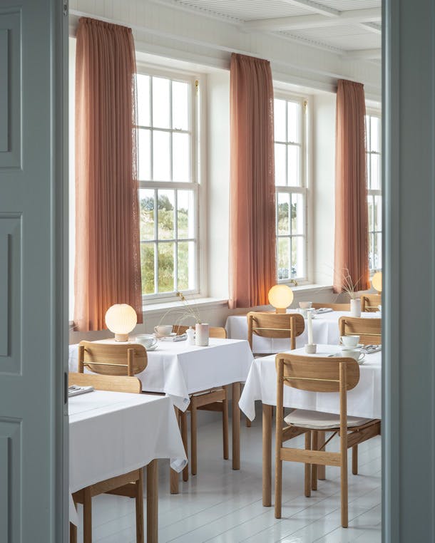 De pastelkleuren van de gordijnen en panelen geven de grote ruimtes kleur, zonder te overheersen. Svinkløv badehotel restaurant met witte houten vloer