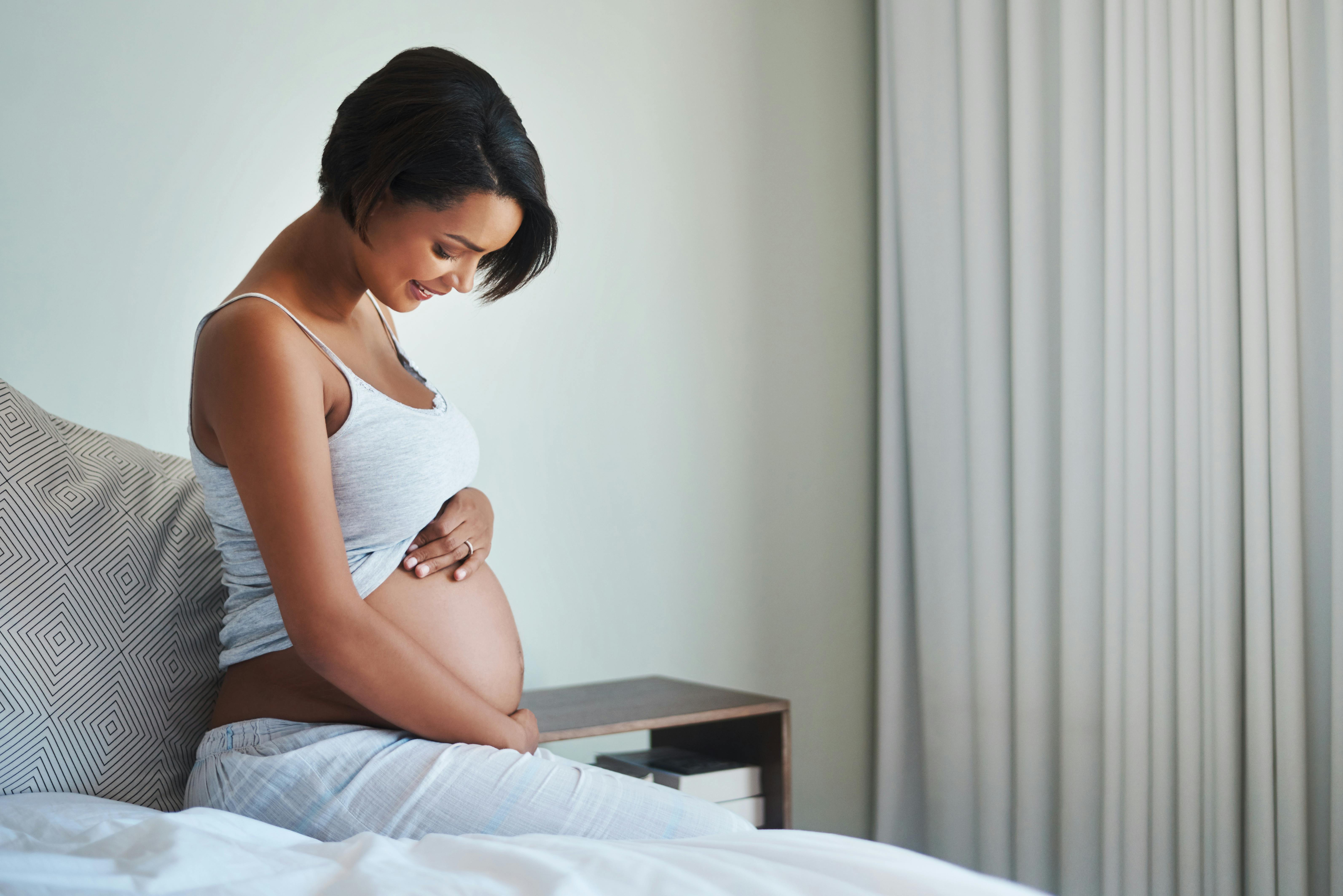 I uge 21 af graviditeten vil du opleve, at bevægelserne bliver mere intense. Kvinde, som er gravid i uge 21, holder om sin mave og sidder i sengen