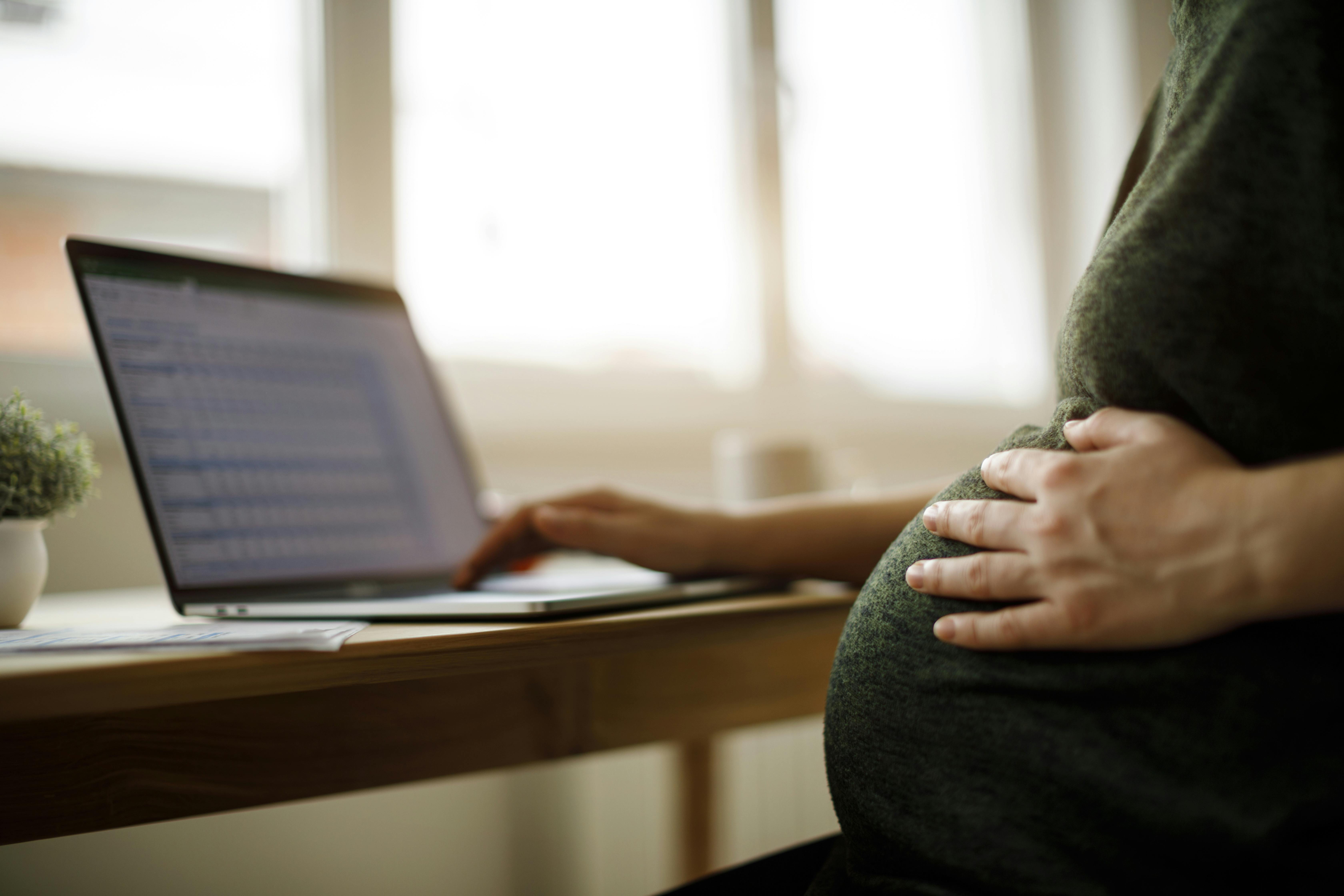 Nu hvor du er gravid i uge 32, er der ikke lang tid til, at du kan tage barsel. Kvinde, som er gravid i uge 32, holder om sin mave, mens hun sidder ved computeren