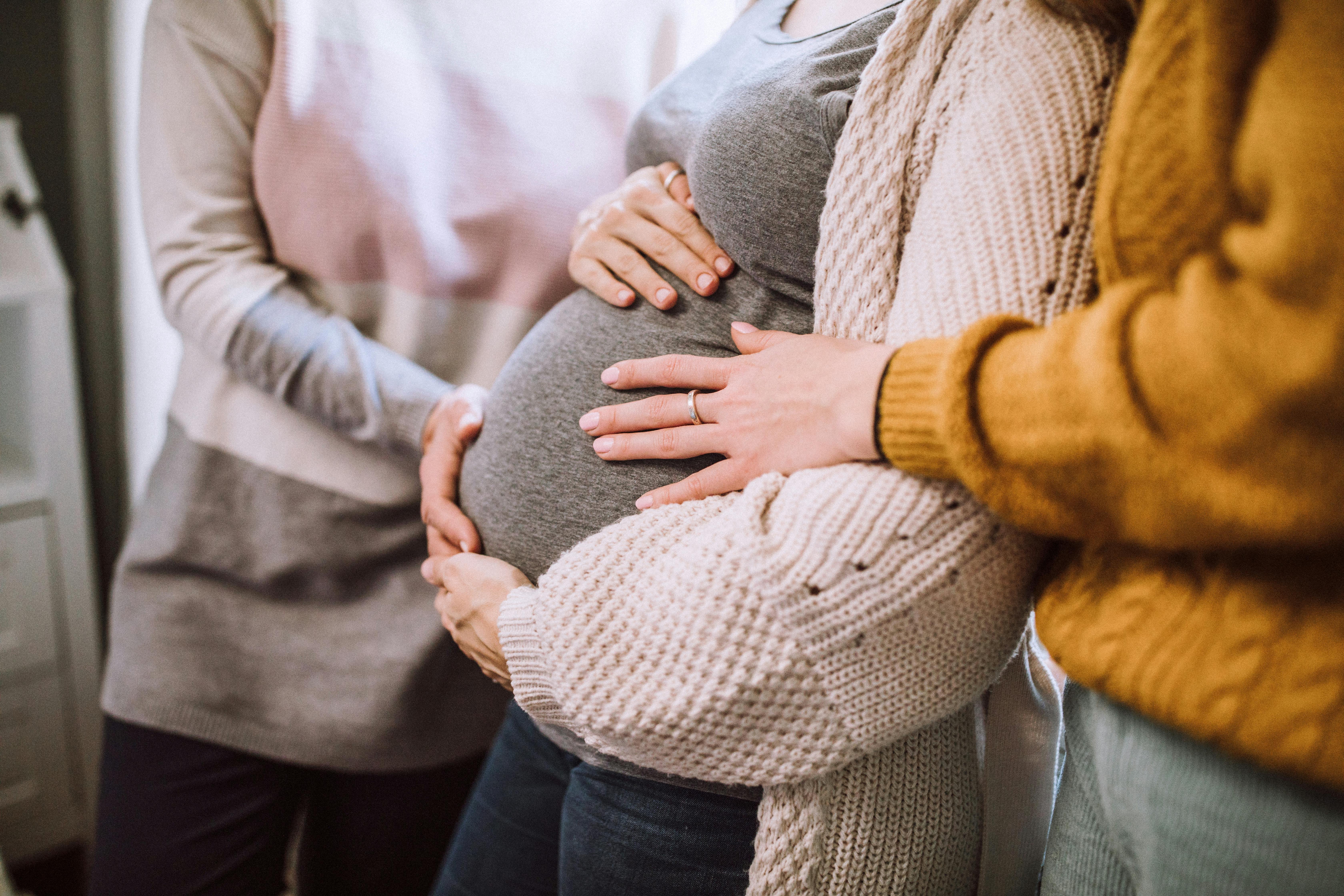 Det kan være svært at få nok med søvn her i uge 34 af din graviditet. Kvinde, som er gravid i uge 34, står med veninder, der holder på maven