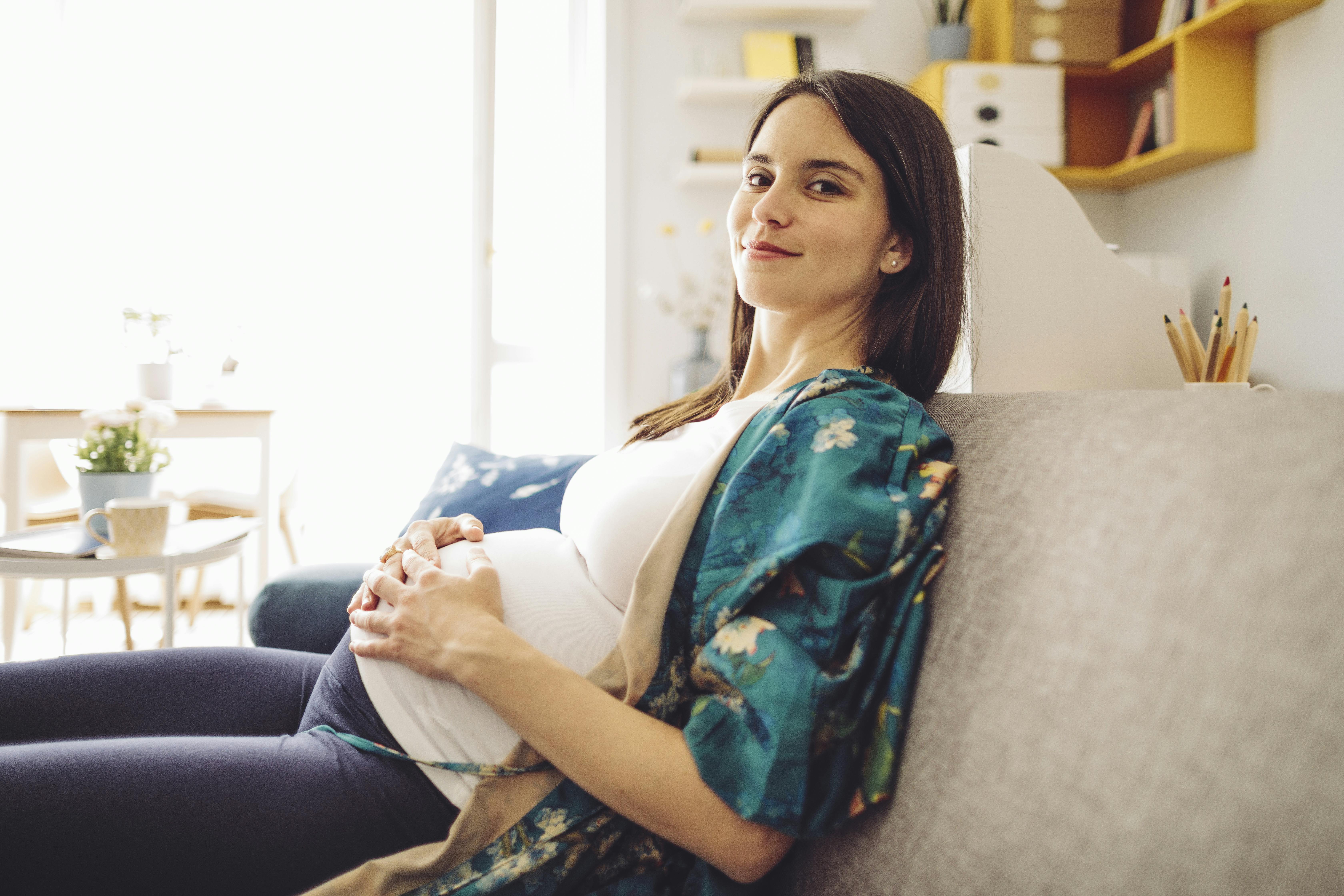 De fleste børn fødes i uge 40 af graviditeten. Kvinde, der er gravid i uge 40, sidder på sofa og smiler mod kameraet